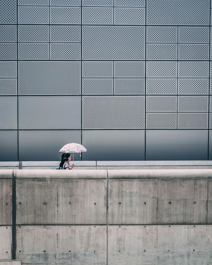 Woman walking with umbrella near modern grey wall in Seoul city, street photography by English teacher from the US.