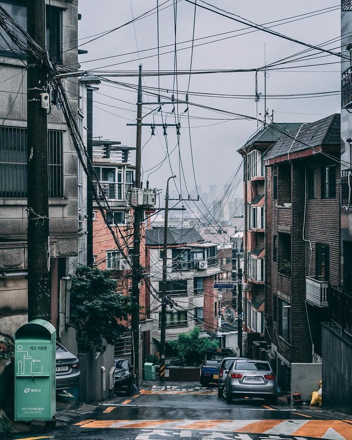 Urban street view in Seoul with residential buildings, cars parked along the road, and overhead electrical wires.