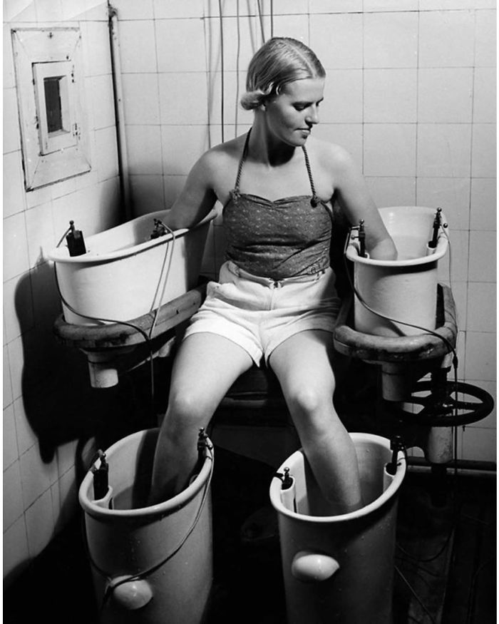 Mujer con brazos y piernas en baños con corriente eléctrica para mejorar la circulación, 1938 aprox.