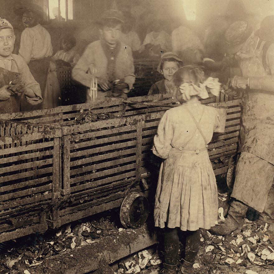 Scene In Canning Factory Showing A 7-Year Old Girl Who Shucks 3 Pots Of Oysters A Day, And Works Regularly, And Her 6-Year Old Brother Who Helps Some. Mostly Negro Workers. The Boss Said "We Keep Only Enough Whites So We Can Control The Negroes And Keep Them Agoing." Location: Bluffton, South Carolina