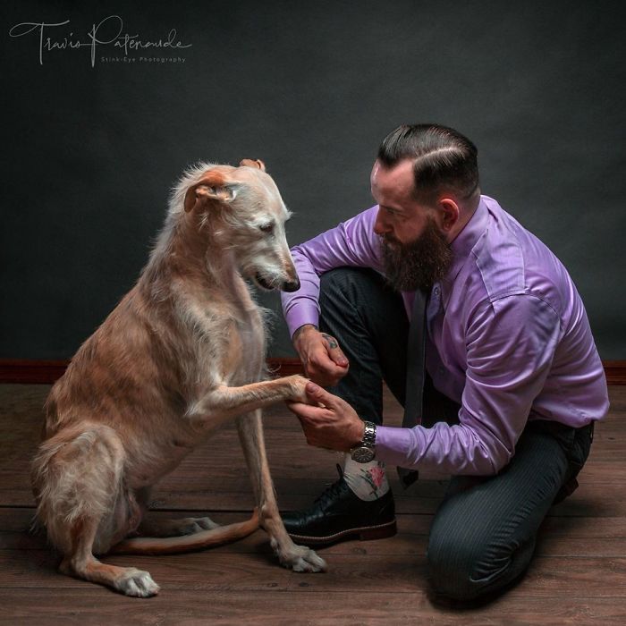 Man kneeling and holding the paw of an abandoned hunting dog in Spain, captured in a heartfelt photo session.