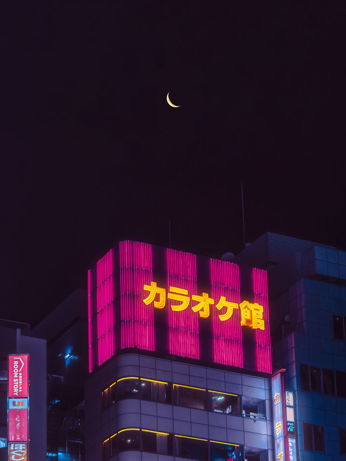 Night view of neon-lit building under a crescent moon in Tokyo, captured during a dream trip photography session.