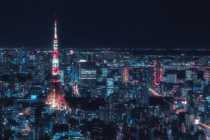 Tokyo cityscape at night with brightly lit buildings and Tokyo Tower glowing in vibrant red and white lights.