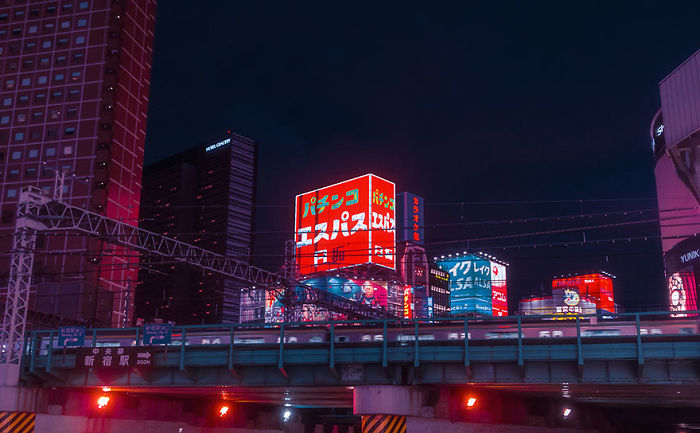 Night cityscape of Tokyo with illuminated neon signs and a train crossing a bridge during a dream trip photography session.