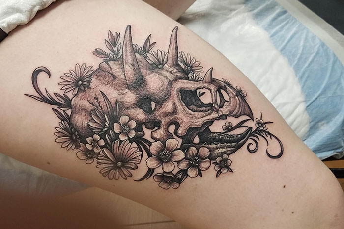 Dinosaur skull with flowers leg tattoo