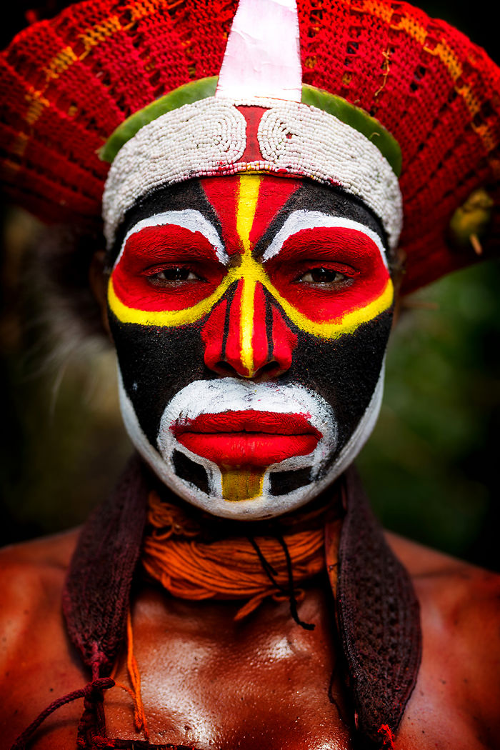 Indigenous person with vibrant traditional face paint and headdress photographed in an inaccessible corner of the world.