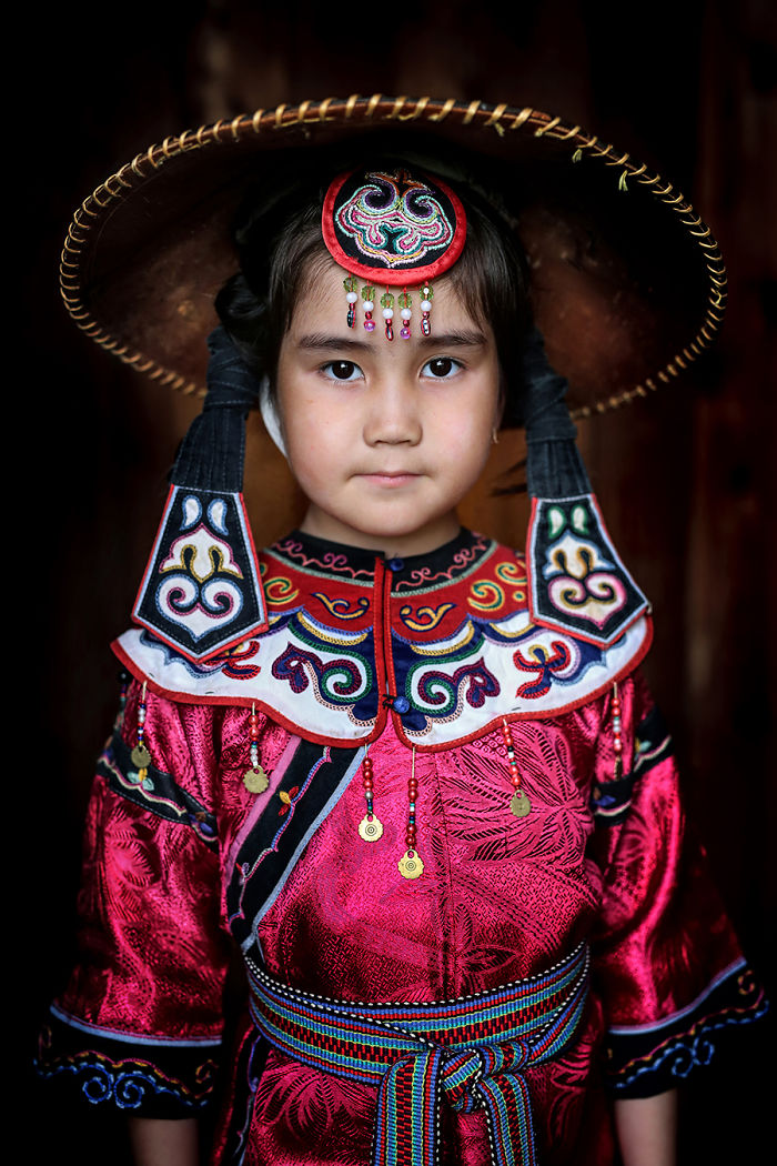 Young indigenous girl wearing colorful traditional attire and hat in an inaccessible corner of the world, photographed closely.