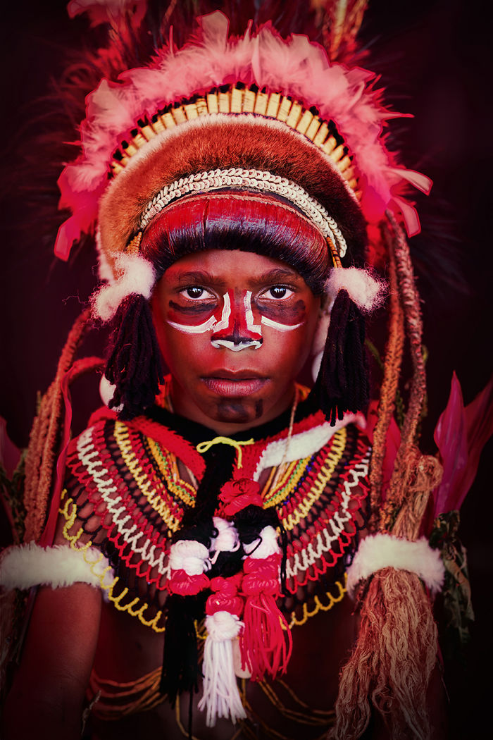 Portrait of an indigenous person wearing traditional face paint and elaborate indigenous clothing and headdress.