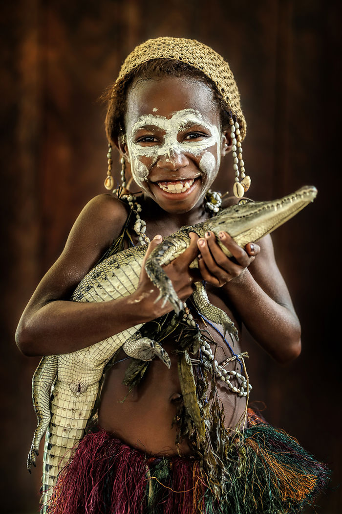 Indigenous child with traditional face paint holding a small crocodile, photographed in an inaccessible corner of the world.