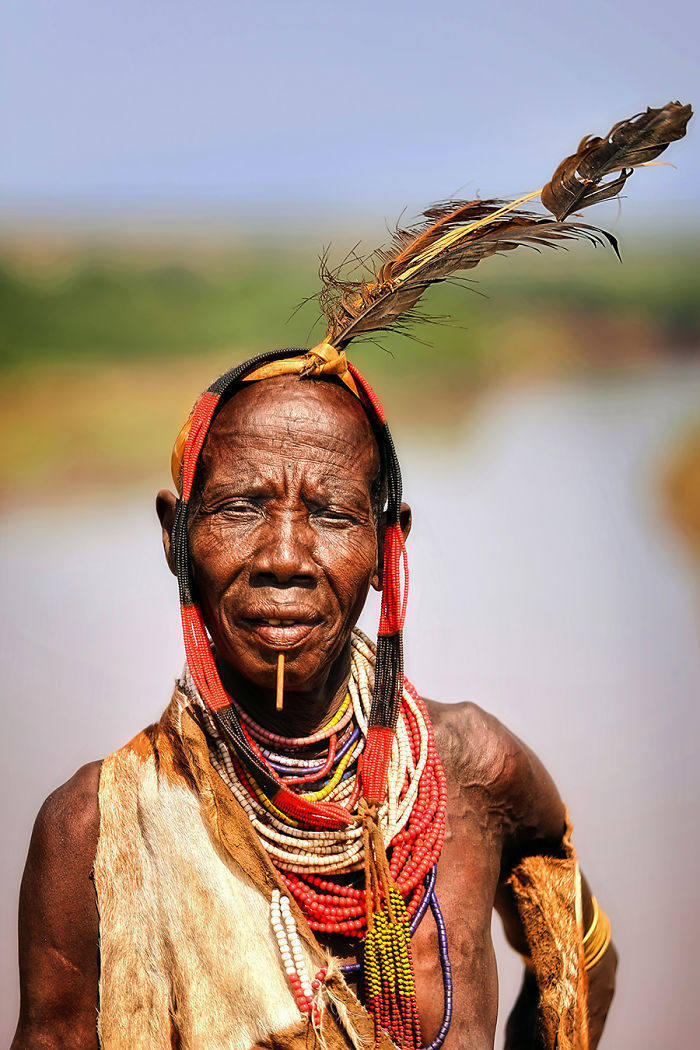 Indigenous person adorned with traditional beads and feathers, photographed in inaccessible corners of the world.