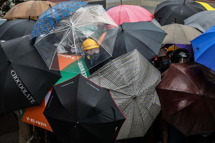 Manifestantes protegiéndose con paraguas los unos a otros contra el gas pimienta que les lanza la policía