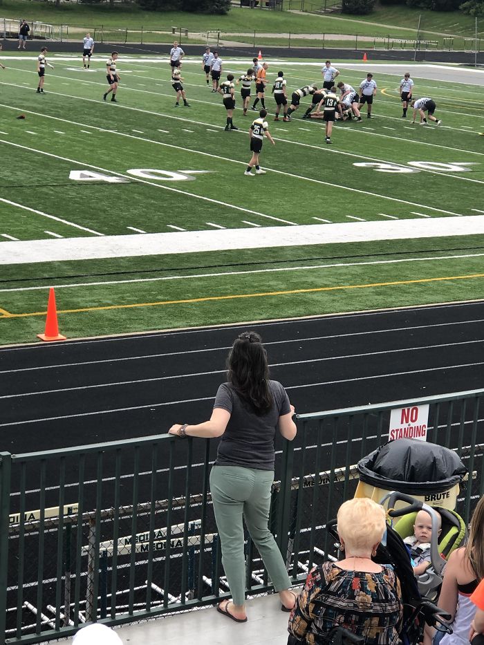 Crazy Parent At A High School Rugby Match. The Sign Says “No Standing On Rail”, This Is So The Handicap Section Can See The Game. She Did Not Listen And Someone’s Poor Grandma Couldn’t Watch Her Grandson Play
