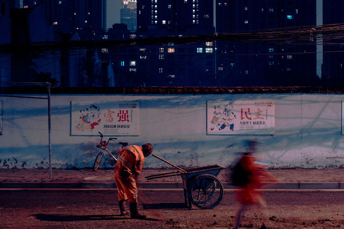 Worker with cart on a dimly lit street near Shikumen lane houses being demolished in Shanghai at night.