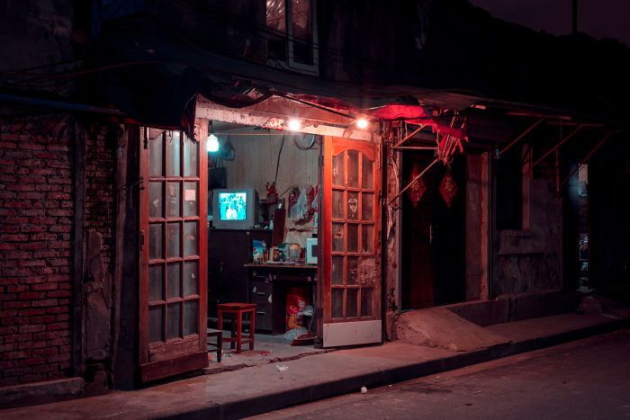 Dimly lit interior of a Shikumen lane house in Shanghai showing old furniture and a glowing television at night.