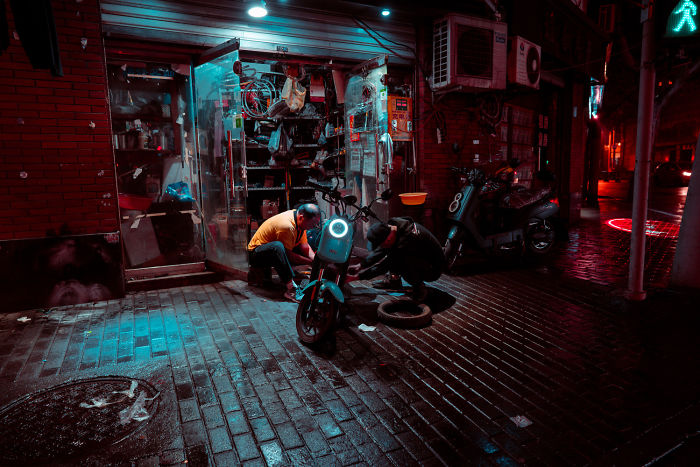 Two men repairing an electric bike outside a Shikumen lane house on a wet night in historic Shanghai streets.