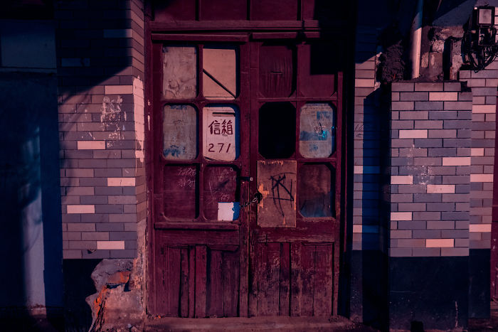 Old Shikumen lane house door in Shanghai with worn wood and faded glass panels in historic neighborhood at dusk.