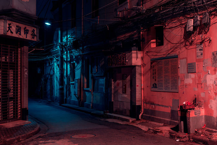 Shikumen lane houses illuminated by red and blue lights on a quiet narrow street in historic Shanghai at night.