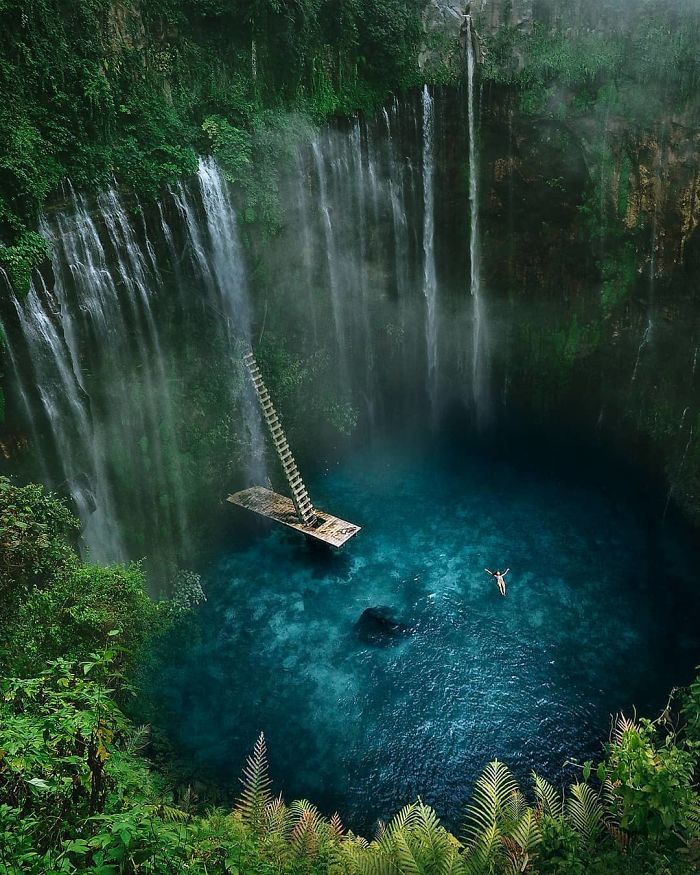 Dreamlike atmosphere with a ladder leading to a floating platform surrounded by waterfalls and lush greenery.