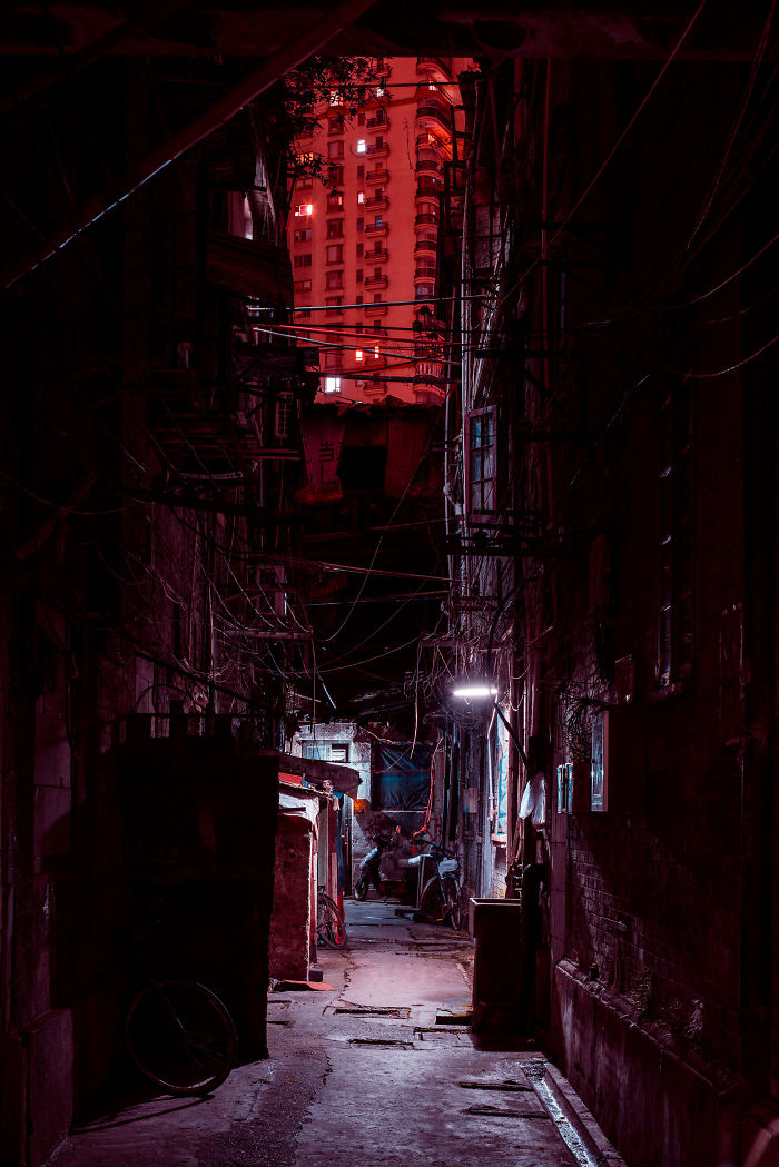 Narrow Shikumen lane houses in Shanghai at night, lit dimly with red tones and visible electrical wires overhead.