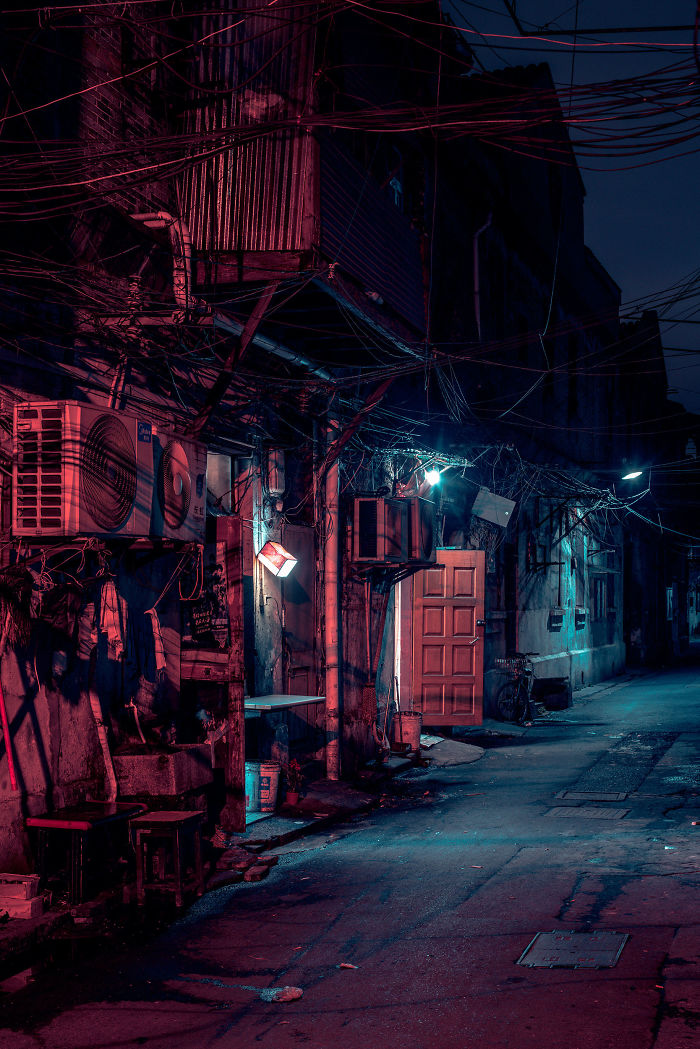 Shikumen lane houses lit by neon lights at night with exposed wiring and air conditioning units in a narrow Shanghai street.