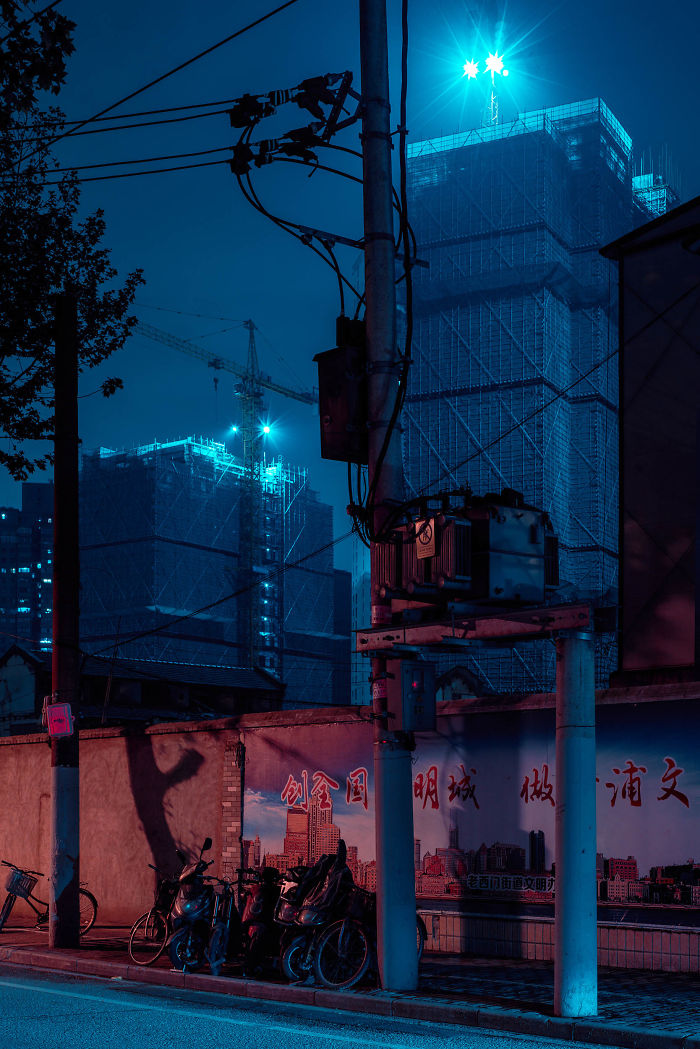 Night scene of Shikumen lane houses and construction cranes in Shanghai with electric poles and parked motorbikes in foreground.