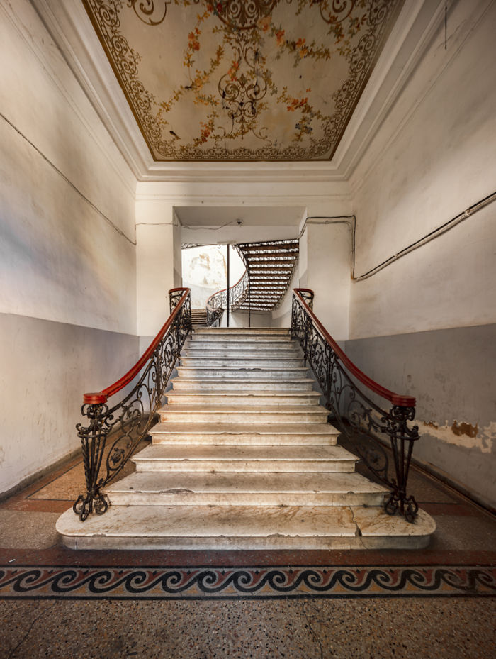 Marble staircase with ornate wrought iron railings and a decorative ceiling in an abandoned place in Tbilisi.