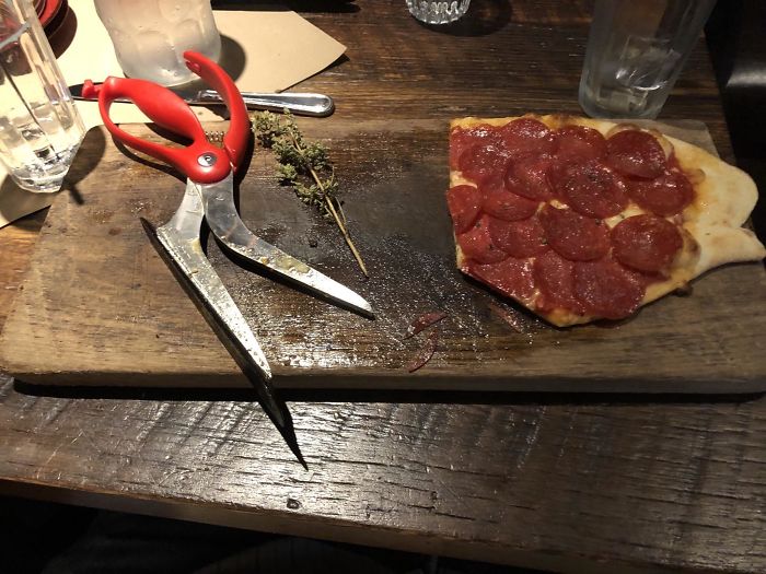Pizza With Scissors On A Slab Of Wood With Historic Grease Soaked In.