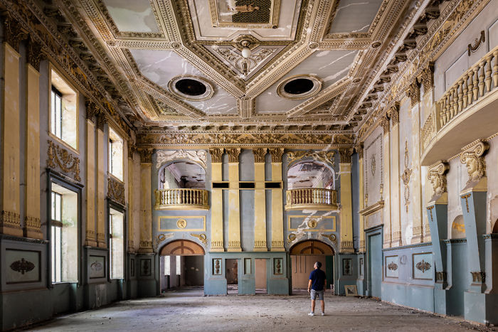 Elegant abandoned interior in Tbilisi with ornate ceilings and a person exploring the historic, decayed architecture of the building.