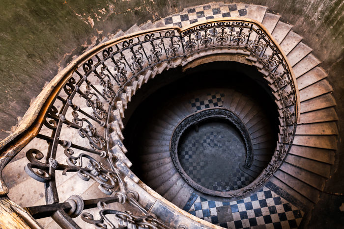 Spiral staircase with ornate railing and worn steps inside an abandoned place in Tbilisi, showing decay and aged architecture.