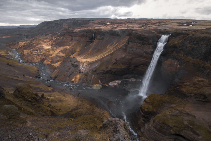 Iceland waterfall cascading into rugged canyon under cloudy sky, showcasing natural beauty of Iceland landscapes.