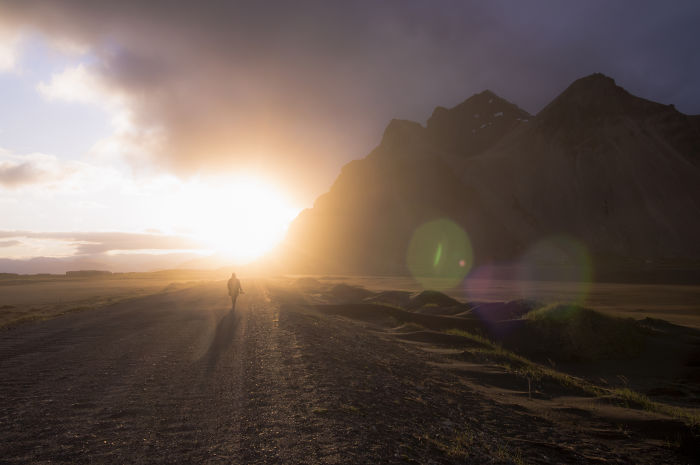 Person walking on a rugged path with mountains and glowing sunlight, showcasing Iceland’s beauty and natural landscape.