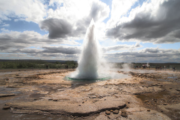 Geyser erupting in Iceland with a cloudy sky, showcasing natural geothermal beauty and rugged landscape.
