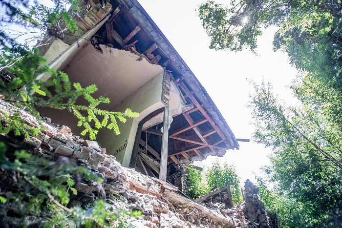 Abandoned thermal baths in Romania showing dilapidated structure overgrown with greenery and damaged roof beams.