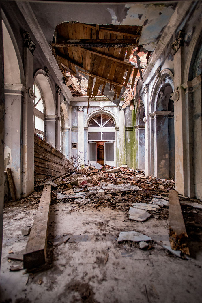 Abandoned thermal baths in Romania with collapsed ceiling and debris scattered in a dilapidated historic corridor interior.
