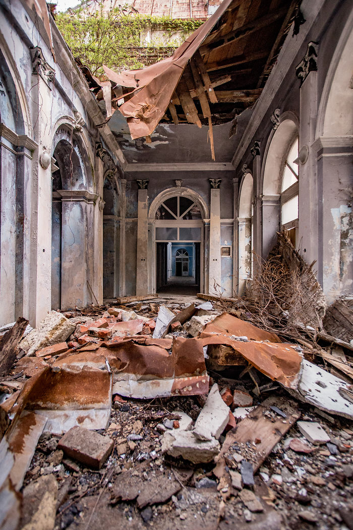Interior view of abandoned thermal baths in Romania showing collapsed ceiling and debris-filled corridor.