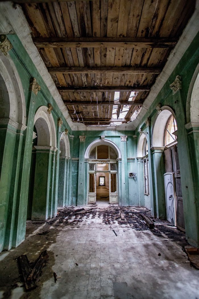 Interior view of abandoned thermal baths in Romania showing deteriorated ceiling and green arches in decay.