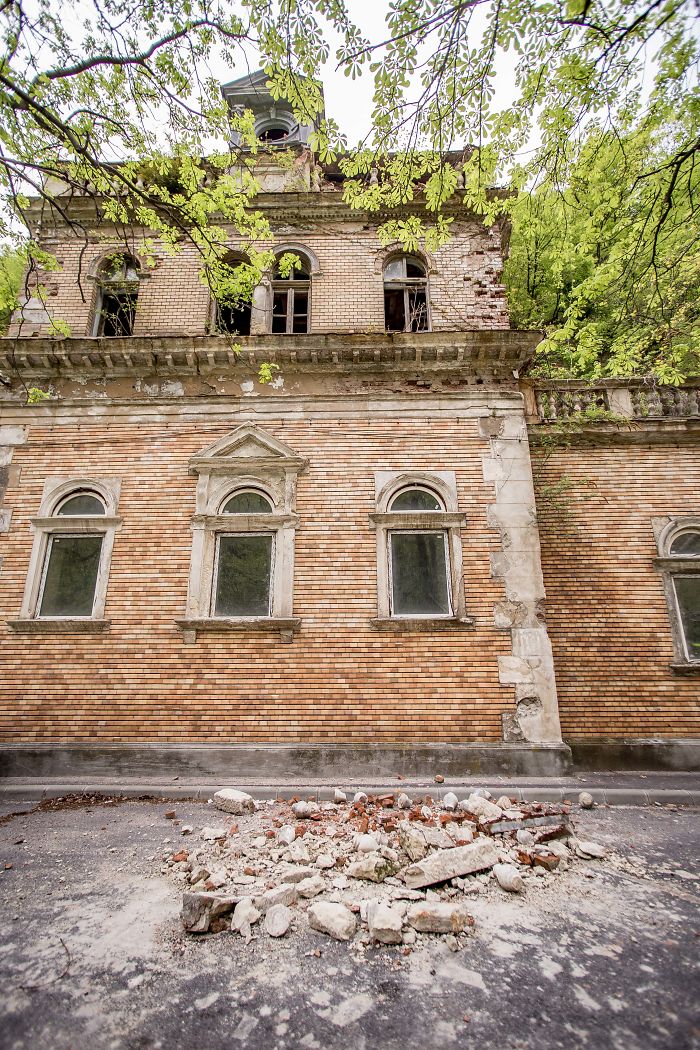 Abandoned thermal baths in Romania showing a decaying brick building with broken windows and rubble on the ground.