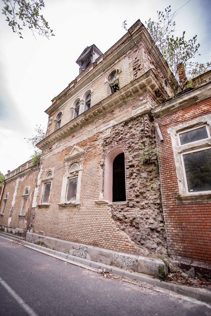 Abandoned thermal baths in Romania showing a deteriorated brick building with broken windows and overgrown plants.