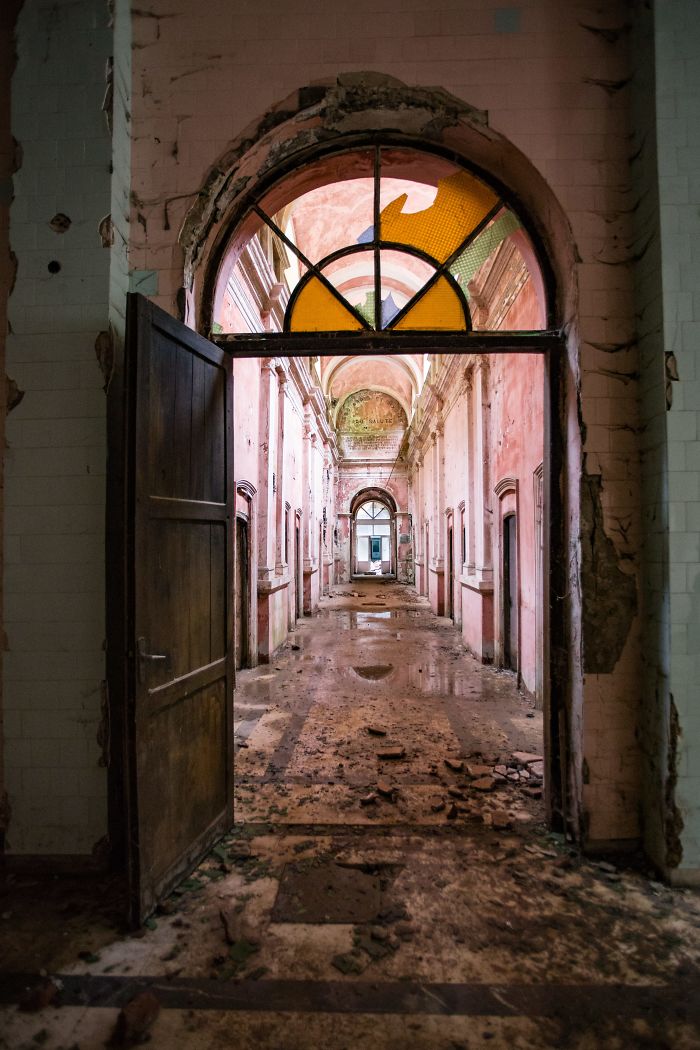 Abandoned thermal baths corridor in Romania showing peeling walls, broken stained glass, and debris on the floor.