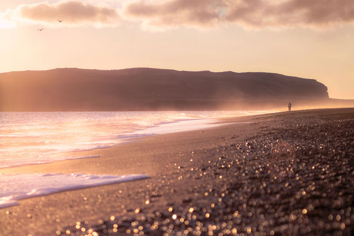 Sunset view of Iceland’s black sand beach with waves and a distant cliff capturing Iceland beauty.
