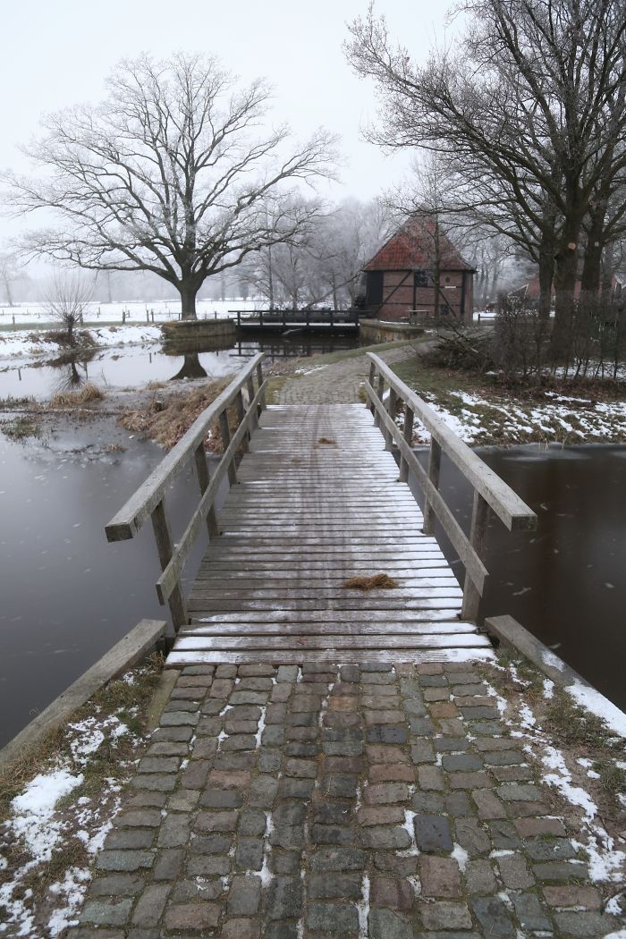 Wooden bridge over a canal in the scenic countryside of a rural area in the Netherlands during winter.