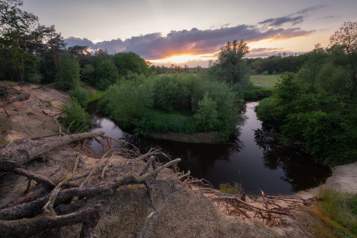 Scenic countryside in a rural area of the Netherlands featuring a winding river, lush trees, and a sunset sky.