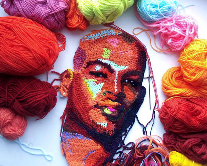 Crochet portrait in progress surrounded by colorful yarn balls, showcasing detailed crochet art and portrait craftsmanship.