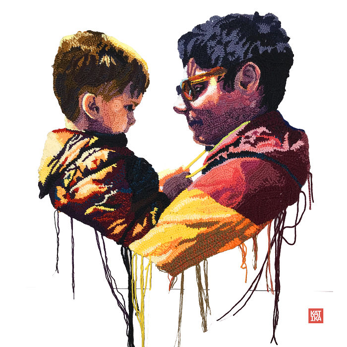 Crochet portrait of a man wearing glasses holding a child, featuring vibrant colors and detailed yarn textures.