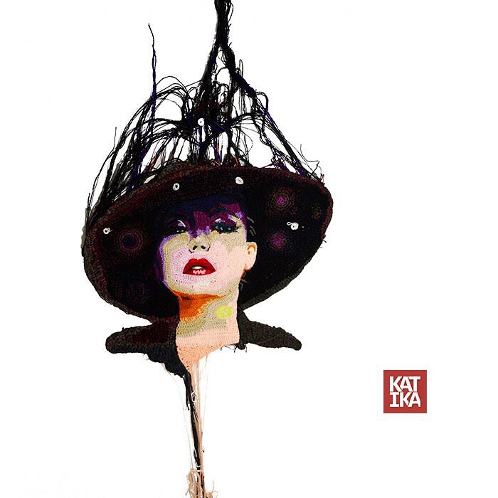 Crochet artist's portrait of a woman wearing a large hat with intricate yarn details and a white background.