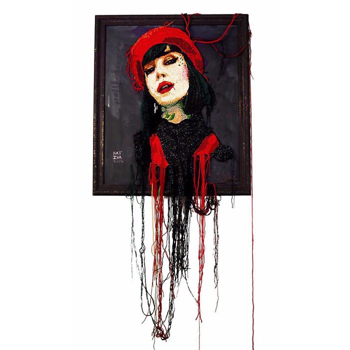 Crochet artist portrait of a woman wearing a red beret with yarn strands hanging from the framed artwork.