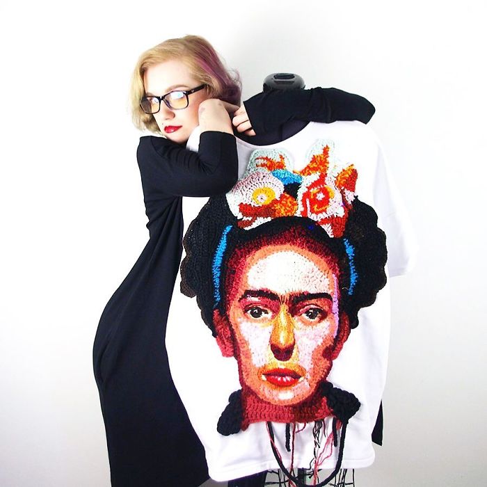 Woman crochet artist posing with a detailed colorful crochet portrait on a white fabric, showcasing artistic yarn work.