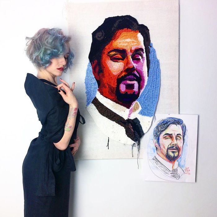 Crochet artist posing next to a colorful crochet portrait and its original drawing of a man with a beard and mustache.