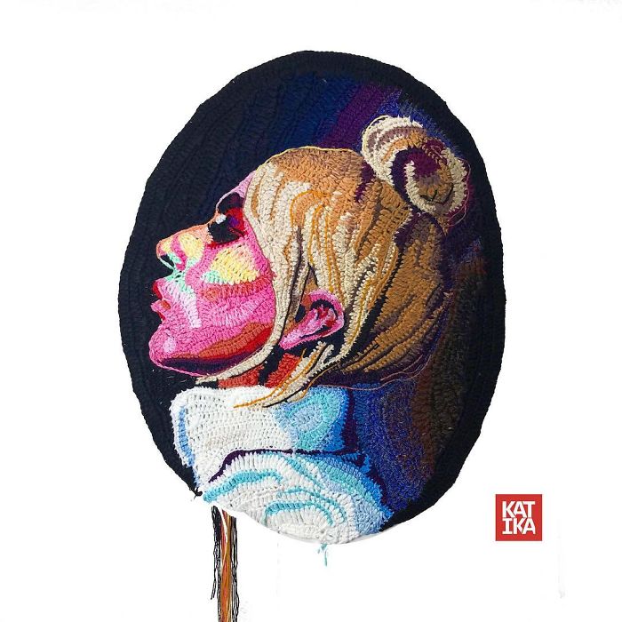 Crochet portrait of a woman with blonde hair in a bun, showcasing detailed colorful stitching and textured fabric art.