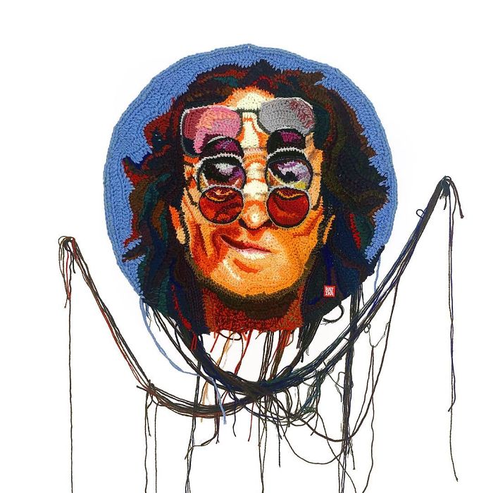 Crochet portrait of a person wearing round sunglasses with colorful yarn details and loose threads hanging below.